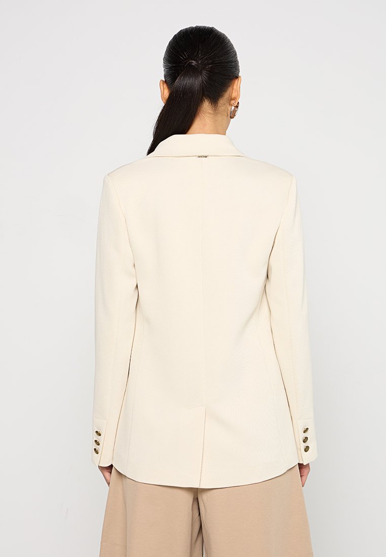 Blazer beige su misura con colletto a scollatura, tessuto strutturato, spacco sul retro e tre bottoni decorativi dorati su ciascun polsino.