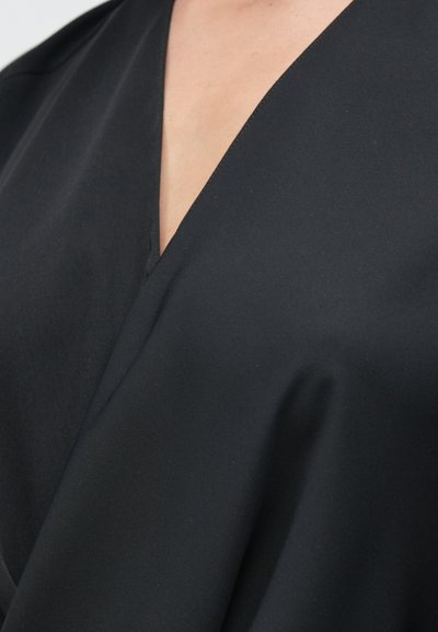 Fekete szövet sima textúrával és finom fényű felülettel, mély V-nyakú kialakítással és a nyakvonalnál hullámzó redőkkel.