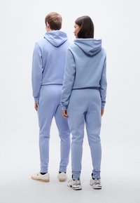 Φόρμες με κουκούλα και παντελόνια jogging σε ανοιχτό γαλάζιο. Το ύφασμα φαίνεται μαλακό με ριμπ μανσέτες και κολαριστό σχέδιο στο φούτερ.