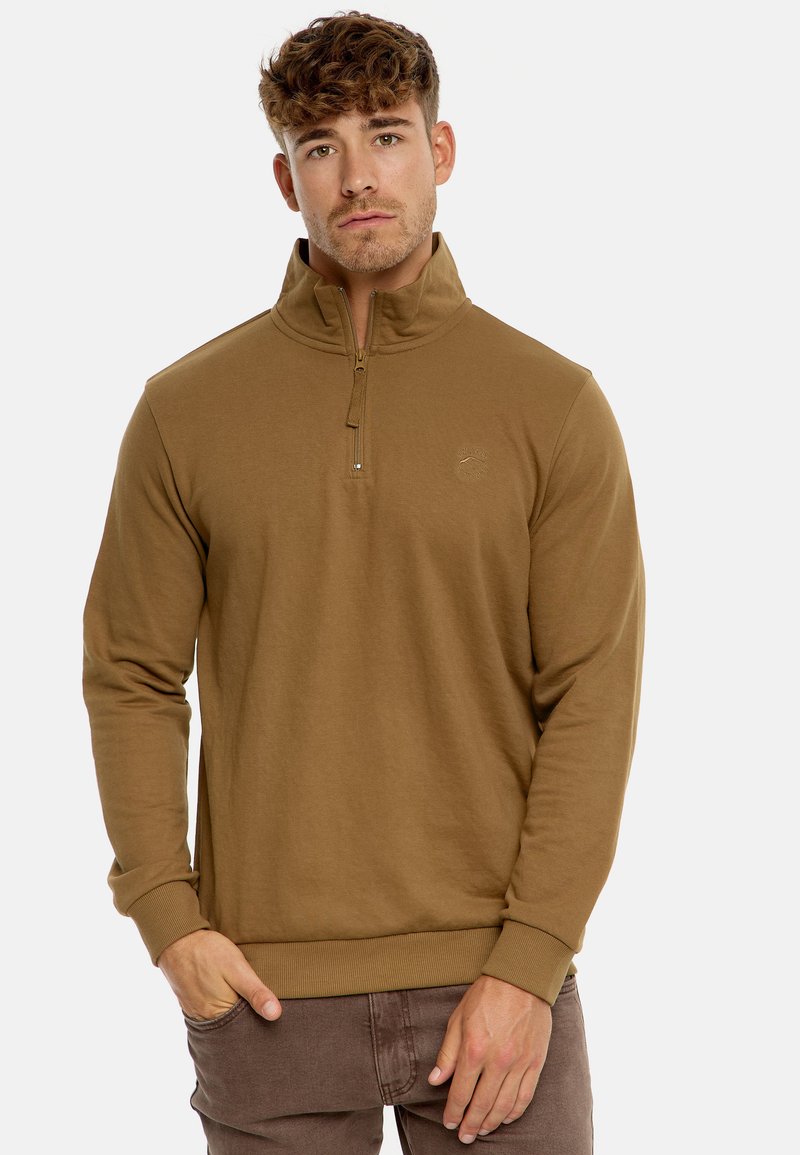 Sweat à zip marron avec un col montant, en tissu doux. Présente des poignets et un ourlet côtelés, avec un petit logo sur la poitrine.