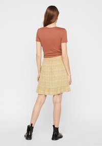 Hnědý top s krátkým rukávem a žlutá sukně s květinovým vzorem a volánkovým lemem. Černé kotníkové boty dokončují vzhled.