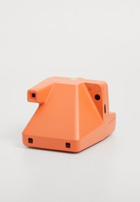 Narancssárga fényképezőgép geometrikus mintával, textúrázott felülettel, látható gombokkal, négyzet alakú lencse nyílással és egy kis színes csíkkal a tetején.