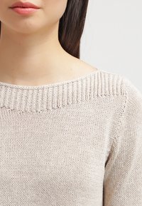 Hellbeige Strickpullover mit weit ausgeschnittenem Ausschnitt, geripptem Kragen und glatter Textur, der eine lässige Passform und minimale Details zeigt.