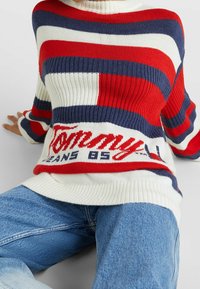 Gestreifter Pullover in Rot, Weiß und Marineblau mit gerippter Textur und oversized Passform. Logotext am Saum sorgt für ein auffälliges Detail.