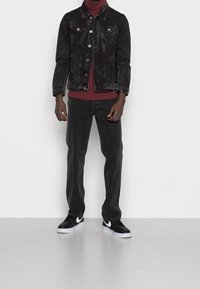 Svart denimjacka med knappstängning och bröstfickor, i kombination med en vinröd polotröja, svarta byxor och svarta sneakers med vita detaljer.