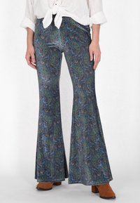 Uitlopende broeken in een donkermarineblauw paisleypatroon met groene en bruine accenten. De stof heeft een gladde textuur. Gemaakt bij bruine laarzen met hak.