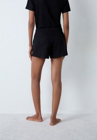 Czarne, lekkie szorty z elastycznym paskiem w talii, gładką fakturą i luźnym krojem, połączone z pasującą czarną bluzką z krótkim rękawem.