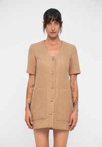 Beige skiftklänning av texturerad tyg, med korta ärmar, en v-ringning och två främre fickor med knappstängning.