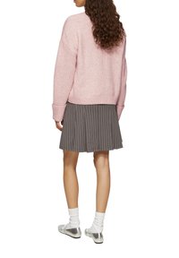 Hellrosa gestrickter Pullover mit überschnittenen Schultern, kombiniert mit einem grauen, plissierten Rock mit weißen Streifen. Silberne Loafers mit weißen Socken.