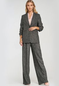 Szary, fakturowany garnitur z dopasowaną marynarką i szerokimi spodniami; jako podkoszulek ma bluzkę bez kołnierzyka w jasnoróżowym odcieniu.