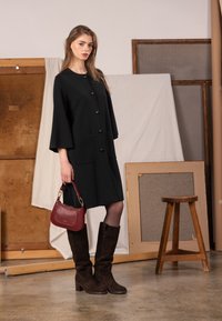 Czarny płaszcz do kolan z dużymi guzikami i kieszeniami, zestawiony z ciemnobrązowymi zamszowymi kozakami do kolan oraz czerwoną torebką. Prosty i elegancki design.