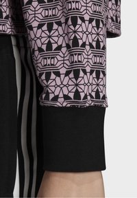 Dlouhý rukáv top s lehce růžovou vzorovanou tkaninou, která obsahuje černé geometrické vzory, spárovaný s jednobarevnými černými manžetami a proužkovanými kalhotami.