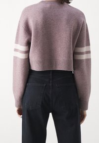 Maglione cropped in lavanda morbido con strisce bianche sulle maniche. Abbinato a jeans neri a vita alta con tasche posteriori.