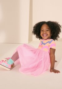 En lekfull klänning med en färgglad top som har abstrakta mönster, kombinerad med en fluffig rosa tyllkjol och rosa sneakers med mintgröna strumpor.