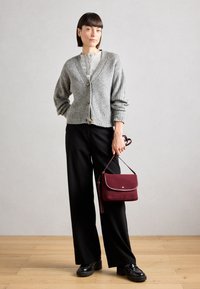 Gilet à côtes gris avec boutons, haut gris, pantalon large noir et sac maroon. Des chaussures à plateforme noires complètent la tenue.