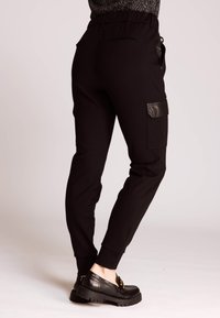 Schwarze Jogginghose mit strukturierter Stoffqualität, elastischem Bund und Lederakzenten. Verfügt über eine seitliche Cargotasche und ein konisch zulaufendes Bein.