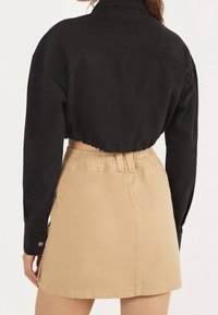 Černá krátká bunda s dlouhými rukávy, s knoflíkovým detailem a nařaseným lemem, v kombinaci s béžovou sukní s vysokým pasem.