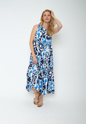 Maxikleid in Blau und Weiß mit gemustertem Design, voluminösem Rock und ärmellosem Schnitt, aus leichtem Stoff gefertigt. Die Sandalen verfügen über flache Riemen.