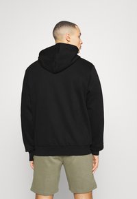 Sudadera con capucha negra de corte relajado, con tejido texturizado y puños acanalados, combinada con pantalones cortos verde claro.