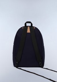 Marinfärgad tygryggsäck med svarta remmar och en beige detalj upptill. Har justerbara remmar och ett handtag på toppen för enkel bärbarhet.