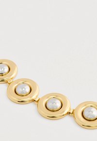 Pulsera de oro enlace con cuatro engastes redondos, cada uno con una cúpula central de plata, sobre un fondo neutro claro.