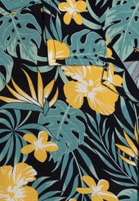 Tessuto di cotone con sfondo nero decorato da vivaci fiori tropicali gialli e bianchi, foglie verdi e motivi intricati.