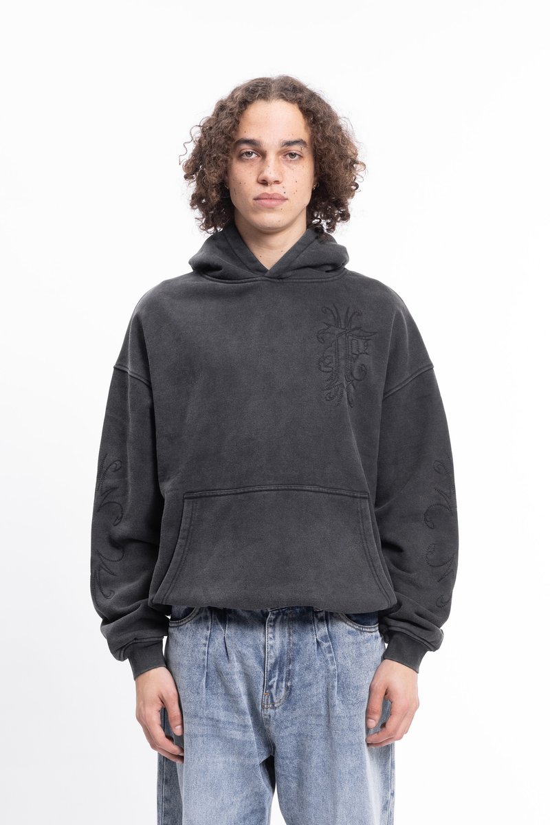 Sweatshirt cinza em tecido suave, com um corte oversized, capuz com cordão e detalhes bordados na parte da frente e nas mangas. Usado com um jeans claro.