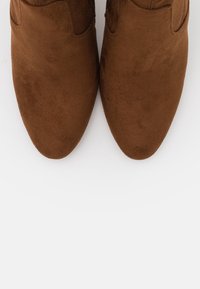 Un par de botas de ante marrón con punta afilada vistas desde arriba sobre un fondo blanco.