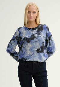 Maglione blu e grigio con un motivo in morbido materiale, con scollatura rotonda e maniche lunghe, abbinato a jeans in denim scuro.