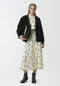 Felpa nera con zip, vestito color crema con motivo a spirale nera, borsa in pelle nera e stivali alla caviglia neri con fibbie.