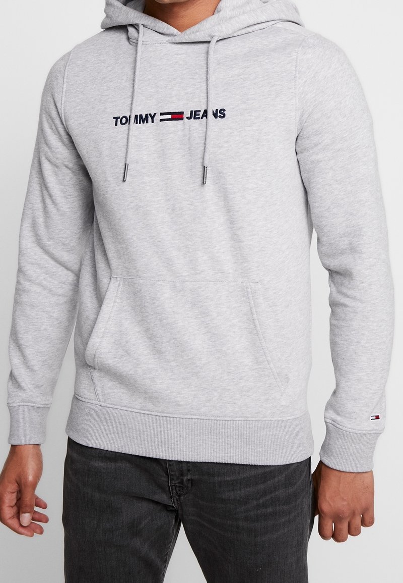 Szara bluza z kapturem, z trokami, kieszenią z przodu, na piersi haftowane logo "TOMMY JEANS" z czerwonymi i niebieskimi akcentami.