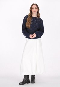 Marineblauwe gebreide trui met open patroon en lange mouwen, gecombineerd met een witte enkellange rok en zwarte enkellaarsjes met gespen.