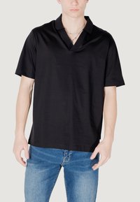 Polo shirt nero a maniche corte con scollatura a V, realizzato in tessuto morbido. Il modello lo indossa con jeans blu, mostrando un look casual.
