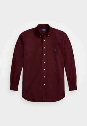 Chemise à manches longues boutonnée en bordeaux foncé avec un col boutonné et un petit logo brodé sur la poitrine gauche.
