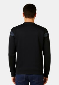 Felpa nera con collo rotondo, polsini e orlo a costine. Presenta due strisce orizzontali blu navy su ciascuna spalla. Texture liscia.
