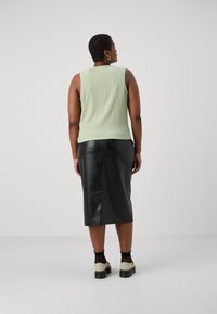 Top sin mangas texturizado en verde combinado con una falda midi de cuero negra. Zapatillas ligeras con acentos negros y calcetas negras transparentes. Diseño simple y moderno.
