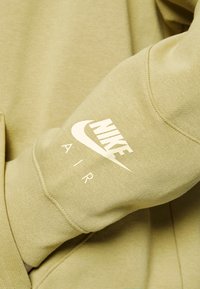 Beige Nike Air sweatshirt sleeve showing the white Nike logo and "AIR" text on textured fabric.
