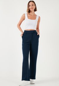 Un crop top blanc et un pantalon large bleu marine avec des poches sur les côtés. Le pantalon présente une texture lisse et des plis avant subtils. Associé à des baskets blanches.