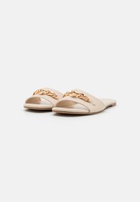 Infradito beige con punta aperta, materiale liscio, decorazione in catena dorata sul davanti, suola piatta con texture minimale.