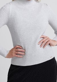 Jasnoszary, prążkowany sweter z golfem i długimi rękawami. Materiał jest miękki, o dopasowanym kroju, z małą metką u dołu.