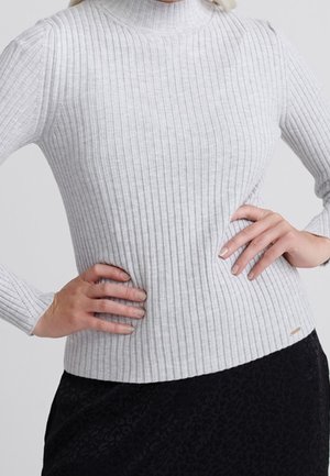 Pull à col roulé côtelé gris clair avec des manches longues. Le tissu est doux avec une coupe ajustée, comportant une petite étiquette sur l'ourlet.