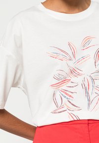 Camiseta de algodón blanca con un estampado de hojas colorido en tonos rojos, melocotón y azules. Diseño de manga corta y corte relajado.