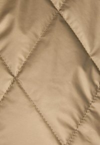 Tessuto beige trapuntato con una superficie liscia, caratterizzato da motivi di cucitura a forma di diamante e una leggera lucentezza. Ideale per capi esterni o isolamento.