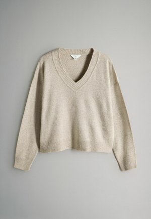 Bežový sveter s výstrihom do V vyrobený z mäkkého materiálu, s poklesnutými ramenami a rebrovanými detailmi na golieri a leme, s krátkym strihom.