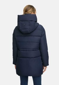 Námorn�ícka puffer bunda s kapucňou, so prešívaným dizajnom, elastickými manžetami a logom na zadnej strane. Hladký, izolovaný materiál.