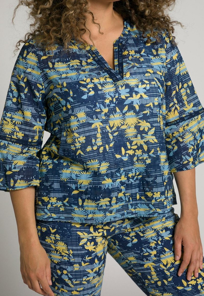 Haut à imprimé floral en marine, jaune et bleu avec un décolleté en V et des manches trois-quarts, complété par un pantalon à motifs assortis. Texture douce.