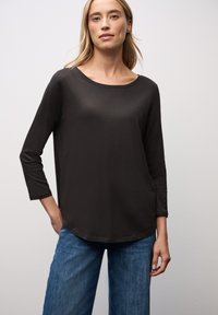 Schwarzes Langarmshirt mit Rundhalsausschnitt und lockerer Passform, kombiniert mit hellblauen, weit geschnittenen Jeans. Glattes Material mit minimalem Glanz.