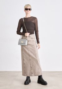 Průhledný černý top s dlouhým rukávem a vzorem houndstooth, spárovaný s béžovou džínovou maxi sukňou a robustními černými kotníkovými botami, nese šedou kabelku.