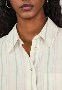 Gaiša svītraina krekla ar pasteļtoņiem (rozā, zaļa, zila) un pogu aizdari, izteiksmīgu apkakli un kreisā krūšu kabatas.