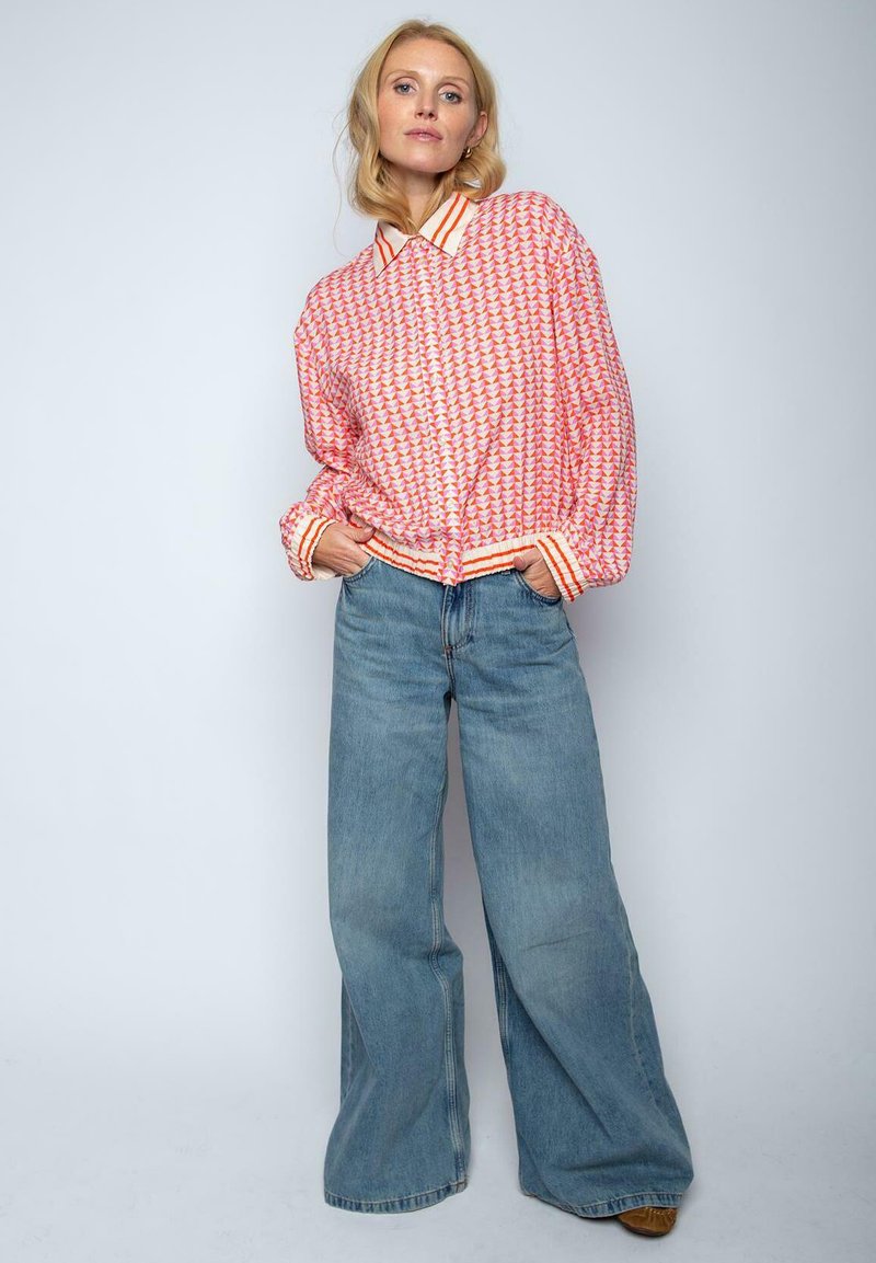 Übergroßes rot-weiß gemustertes Hemd mit gestreiftem Kragen, kombiniert mit weit geschnittenen hellblauen Jeans. Lässig, entspannte Passform.